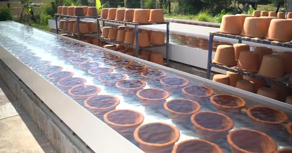 Rows of unglazed ceramic water filter pots drying on racks and in trays outside the Hydrologic factory