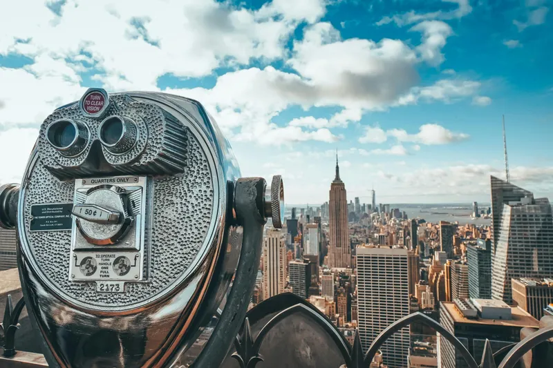 View of New York City skyline featuring iconic Empire State Building with observation binoculars in the foreground.